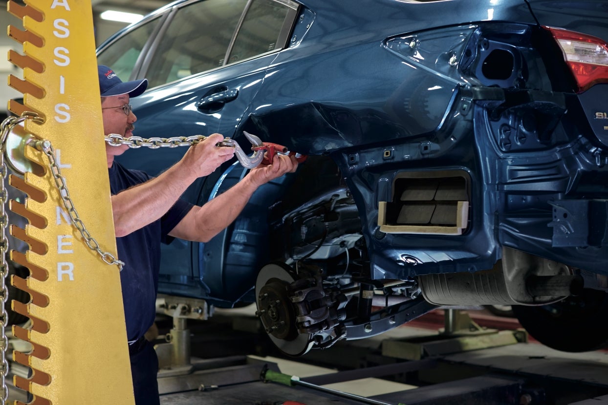 A mechanic uses a chain on a chassis liner to repair the rear-end damage of a blue car.