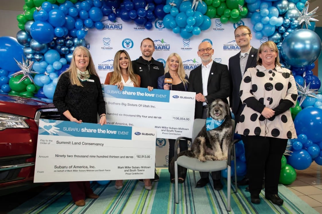 Mark Miller Subaru team presenting oversized Share the Love donation checks alongside a dog