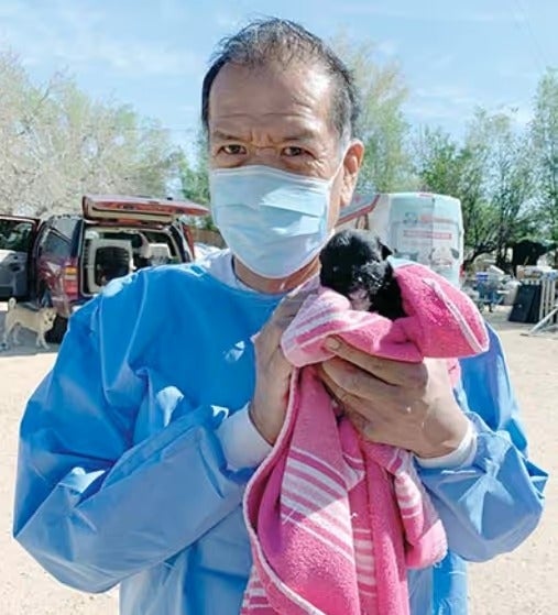 Volunteer in protective gear holding a rescued puppy wrapped in a blanket