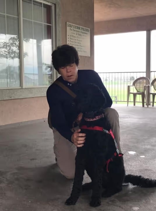 A person kneeling beside a trained service dog