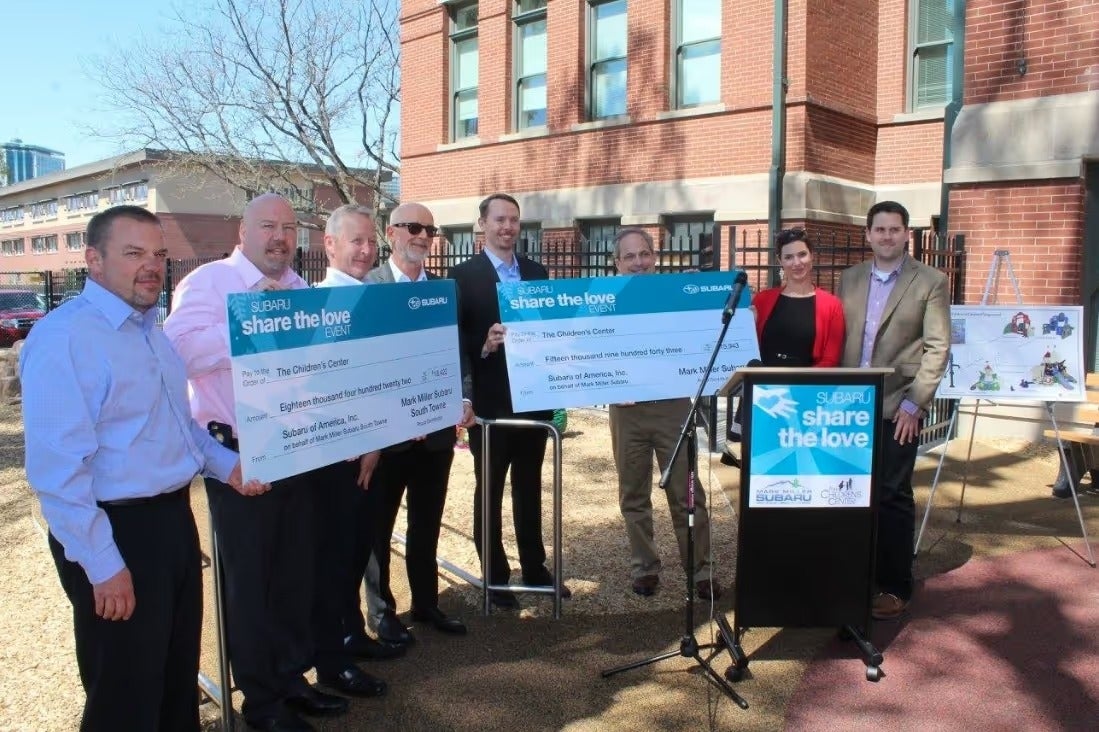 Group holding oversized Share the Love donation checks at an outdoor presentation