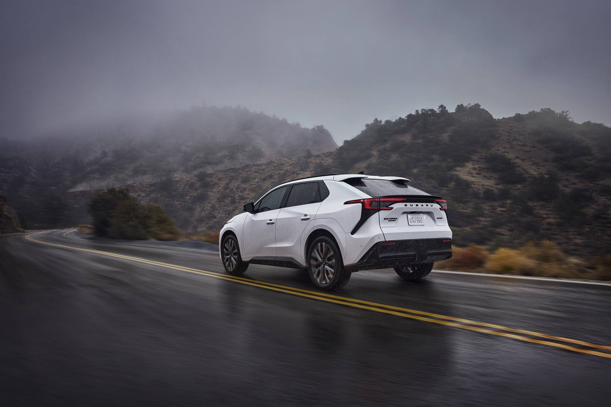 2026 Subaru Solterra in white on a wet mountain road in fog, rear three-quarter view