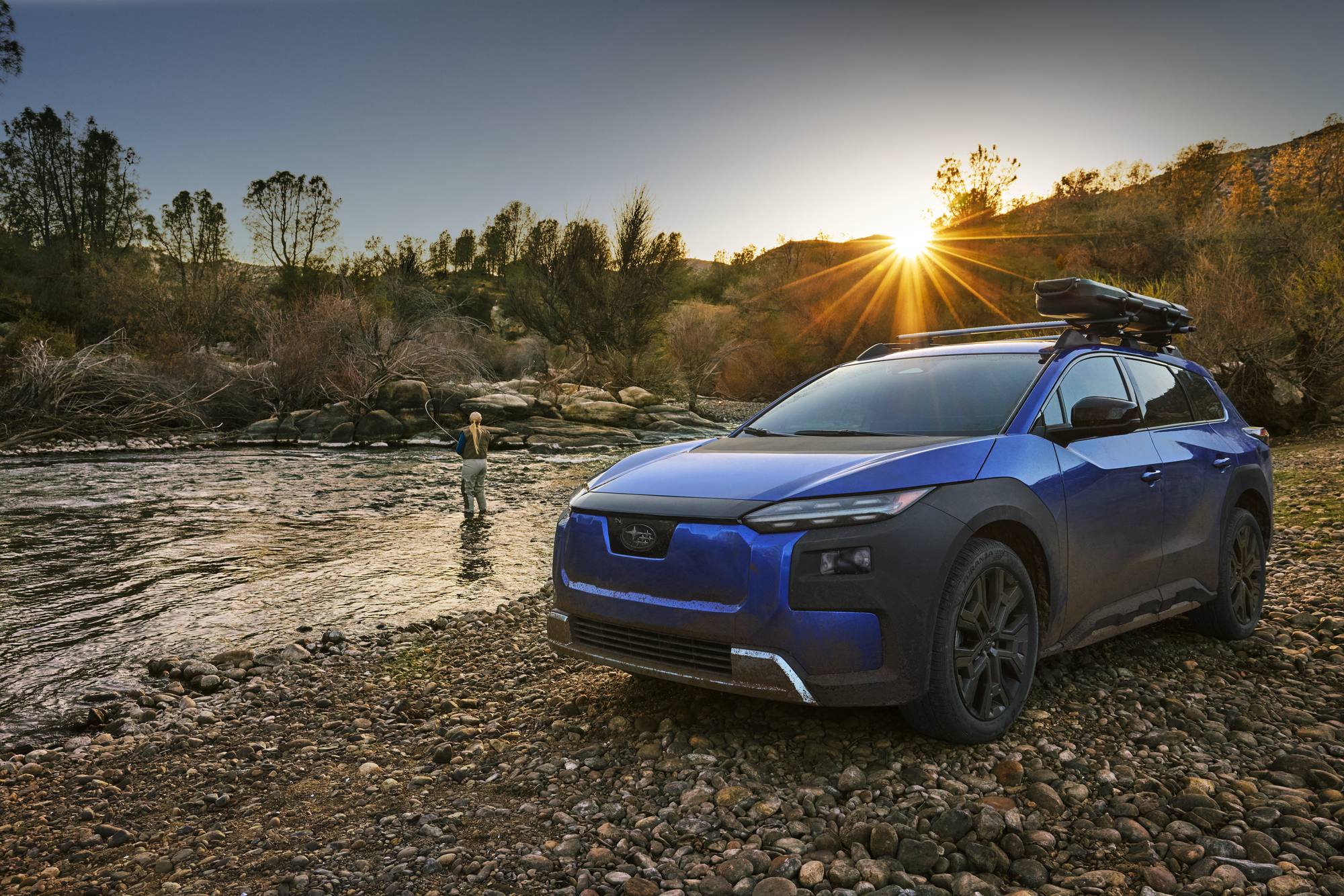 2026 Subaru Trailseeker in blue parked on a river bed at sunset with a roof cargo box